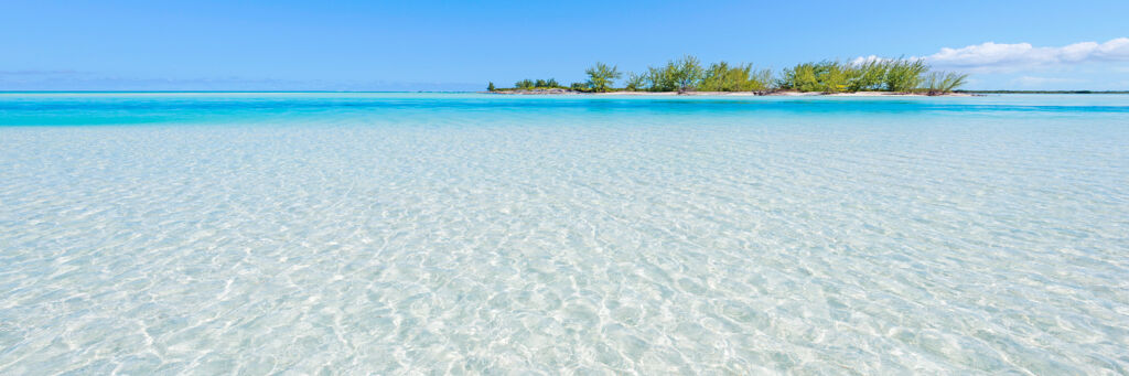 Clear waters of Horsestable Beach on North Caicos, with a small island in the distance.